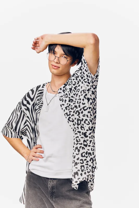 young man posing in casual leopard and zebra print shirt with glasses, white t-shirt, and relaxed expression on white background