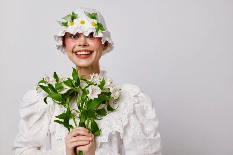 Cheerful woman in white vintage dress holding flowers, exuding joy and positivity against a neutral background, perfect for seasonal themes