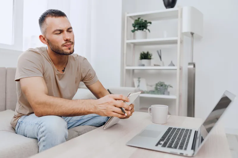 Thoughtful man using a smartphone while sitting on a cozy sofa in a modern living room, reflecting a stylish and relaxed lifestyle in 2025 trends.