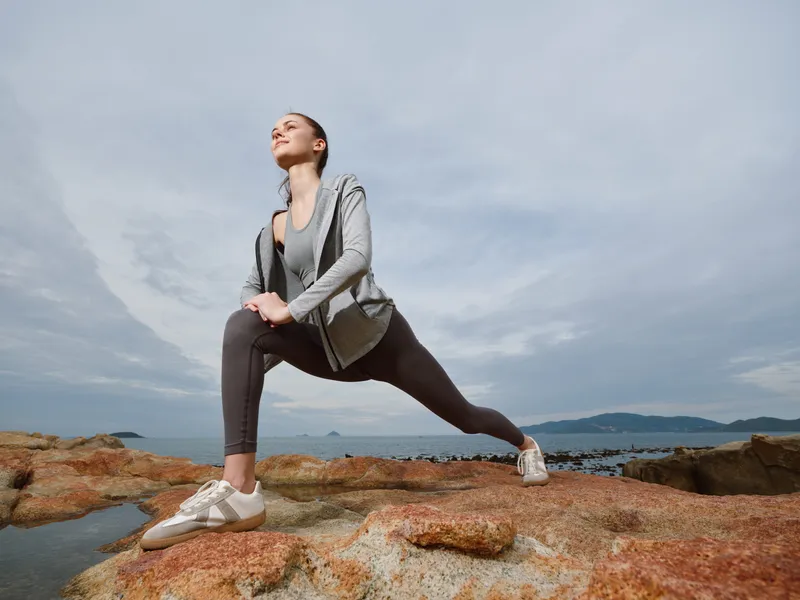 Athletic woman practicing yoga poses on rocky beach, showcasing strength and relaxation in outdoor workout attire with a serene backdrop