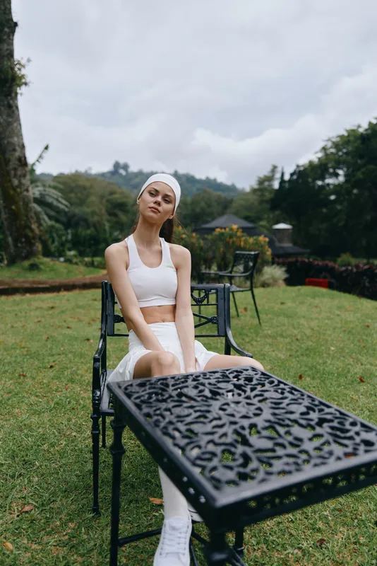 Young woman in activewear relaxing outdoors on a stylish black metal chair surrounded by greenery, embodying a serene and healthy lifestyle
