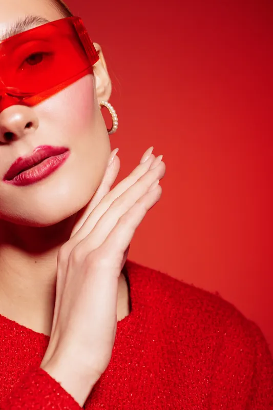 Close-up of a stylish woman wearing red sunglasses and red lipstick posing against a red background. Concept of fashion, beauty, and modern style with vibrant colors.