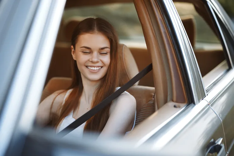 Happy young woman enjoying a road trip in a car, smiling with eyes closed, wearing a casual outfit, emphasizing joy and freedom.