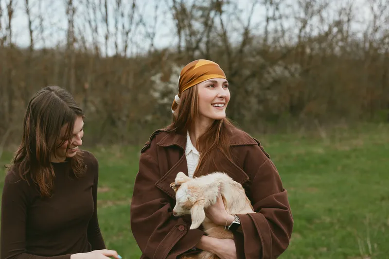 Goat kid outdoor lifestyle woman friend meadow nature scene captured in a sunny field, candid moment of joy and companionship as the pair interact with the gentle animal
