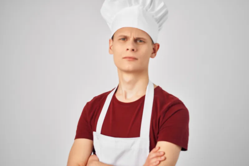 Профессиональный повар-мужчина в белом фартуке на кухне, передающий эмоции