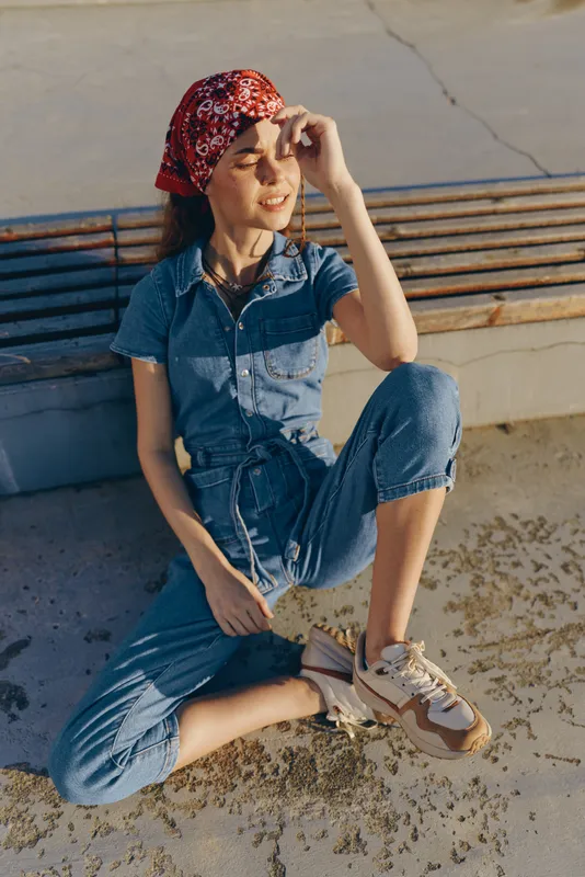 Lifestyle woman in modern boho-western denim street style wearing a red bandana and sneakers, enjoying warm sunlight with a relaxed and casual vibe in film color.