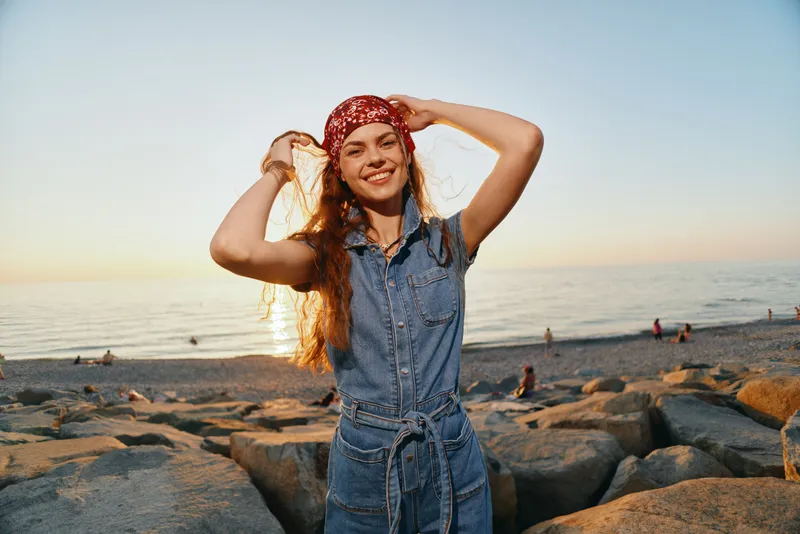 lifestyle woman in modern boho-western denim street style smiling by the beach at sunset with warm film color tones and relaxed joyful vibe