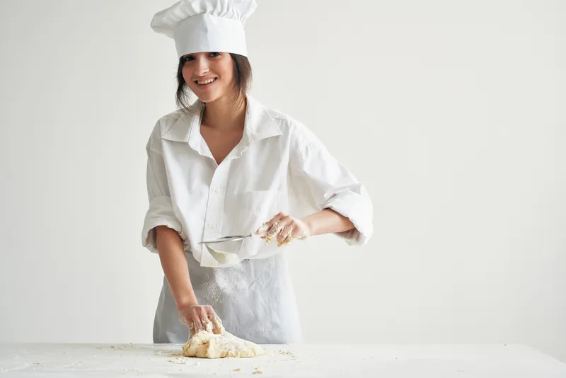Женщина в форме повара, пекарь раскатывает тесто, работа на кухне