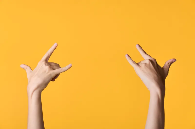Two hands form a rock sign gesture against a vivid orange background, conveying energy, confidence, and musical attitude, perfect for lifestyle, youth culture, and event themed projects.