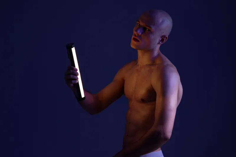 Intense man holding a light in a dark setting, showcasing dramatic shadows and vibrant contrast. A striking contrast enhances the overall mood of the scene.