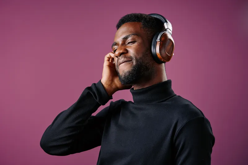 Young Black man enjoying music with headphones against a purple background, expressing joy and relaxation through his posture and facial expression