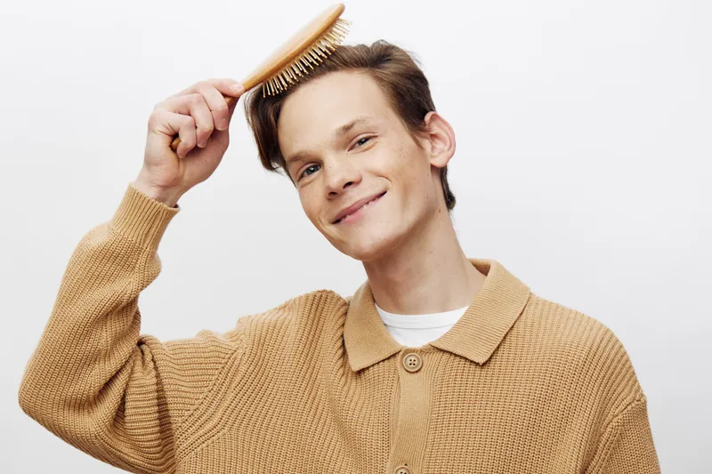 Улыбающийся молодой человек укладывает волосы расческой