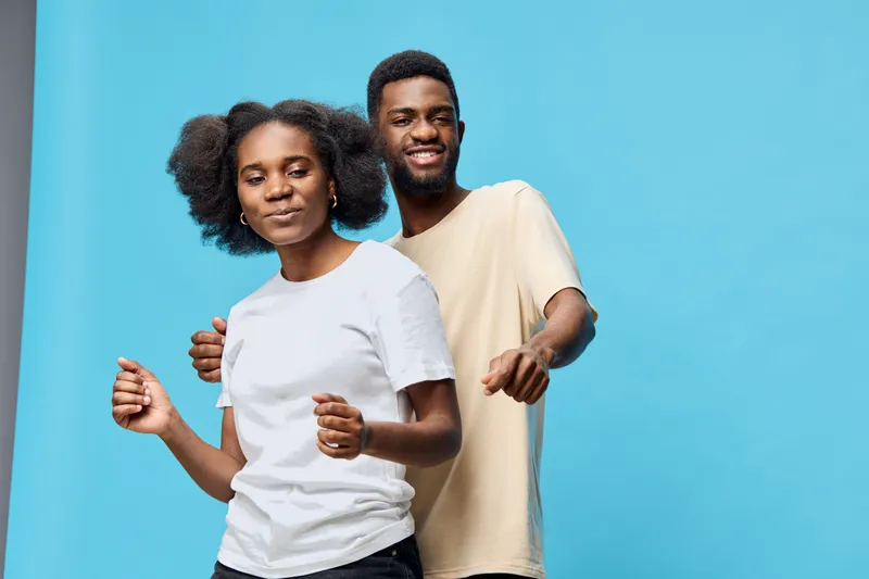 Happy couple dancing together against a blue background, showcasing joy and connection, wearing casual clothing that highlights modern fashion trends