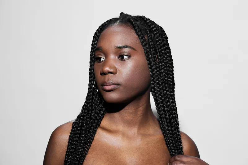 Portrait of a young Black woman with long braided hair, showcasing confidence and grace against a minimalist white background