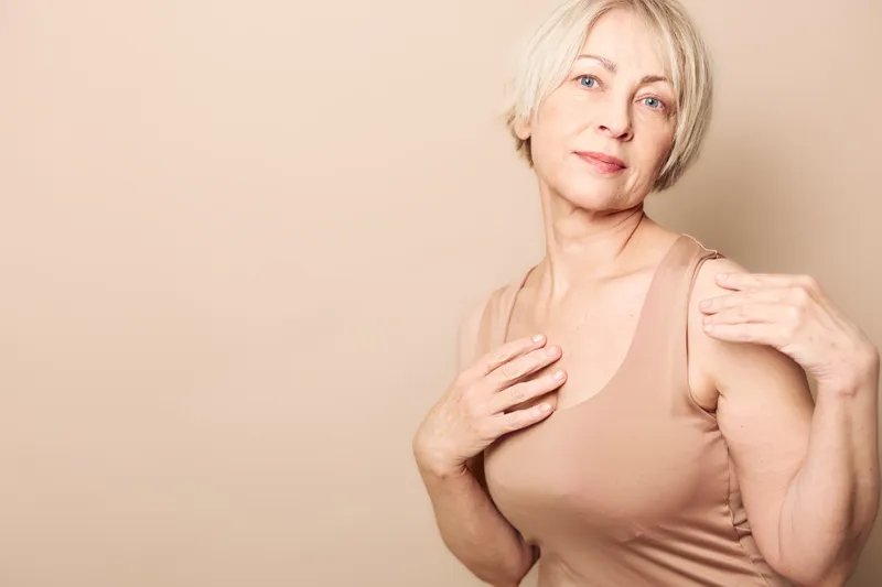 Portrait of a mature woman with short blonde hair wearing a beige tank top, posing against a neutral background. Concept of natural beauty, confidence, and aging gracefully.