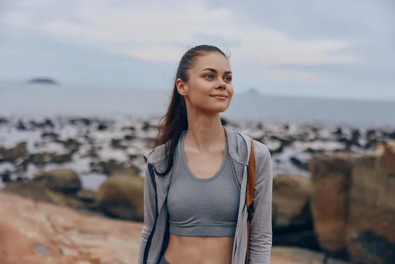 Young woman in sporty outfit enjoying nature by the sea, exuding confidence and happiness, ideal for healthy lifestyle and fitness concepts