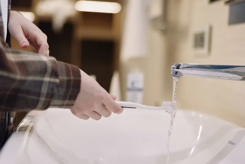Hands at a modern faucet releasing water into a white sink, close up, hygiene scene in a bathroom, emphasizing cleaning, wash routine, freshness and practical home care for daily rituals and