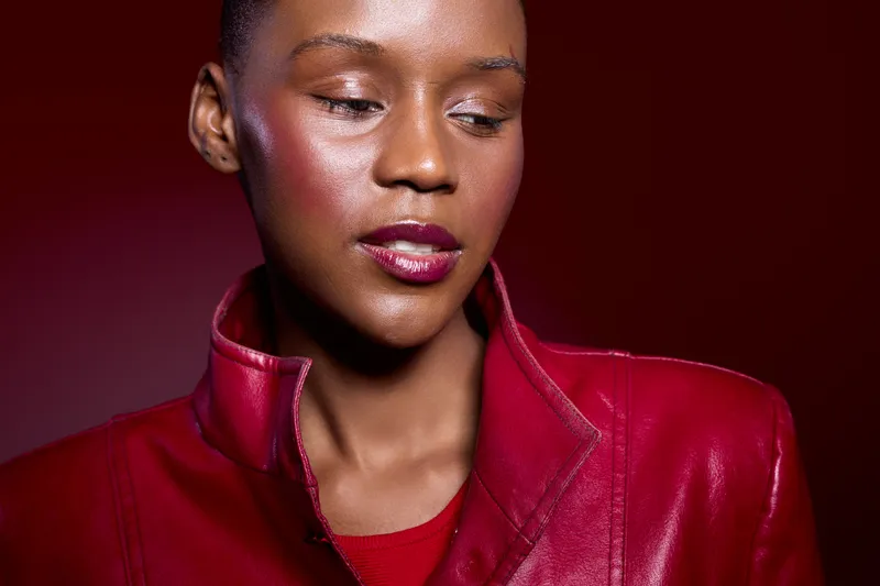 Close-up portrait of a young black woman with dark skin wearing a red leather jacket on a red background. Concept of fashion, beauty, and confident female model in studio lighting.
