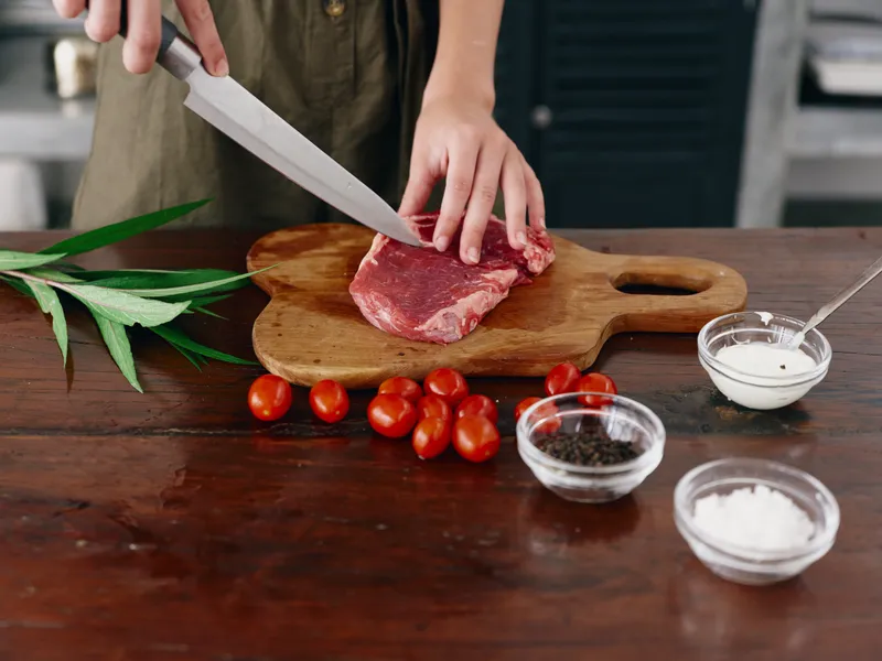 Женщина с ножом в руке нарезает мясо стейка для жарки на кухне