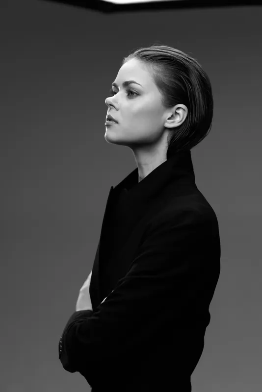 Black and white portrait of a thoughtful woman in a dark coat with braided hair against plain background
