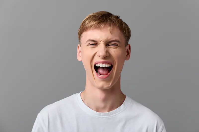 Excited man shouting with a wide mouth in a white tee, studio background, expressive energy and bold emotion captured in a closeup headshot style, without branding