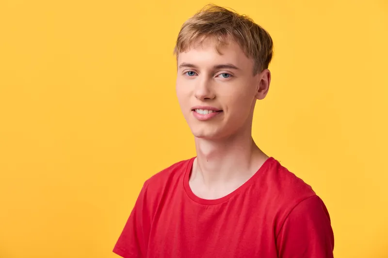 Smiling man in a red shirt stands against a vibrant yellow background, casual studio setup, relaxed pose, bold color palette ideal for lifestyle, fashion and advertising use.