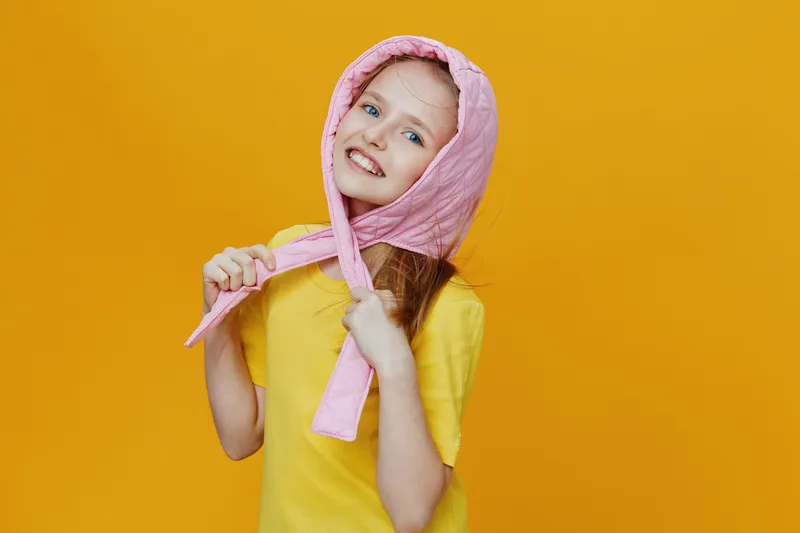 Happy girl wearing a pink headscarf on a vibrant yellow background, showcasing a playful and cheerful mood in a colorful summer setting