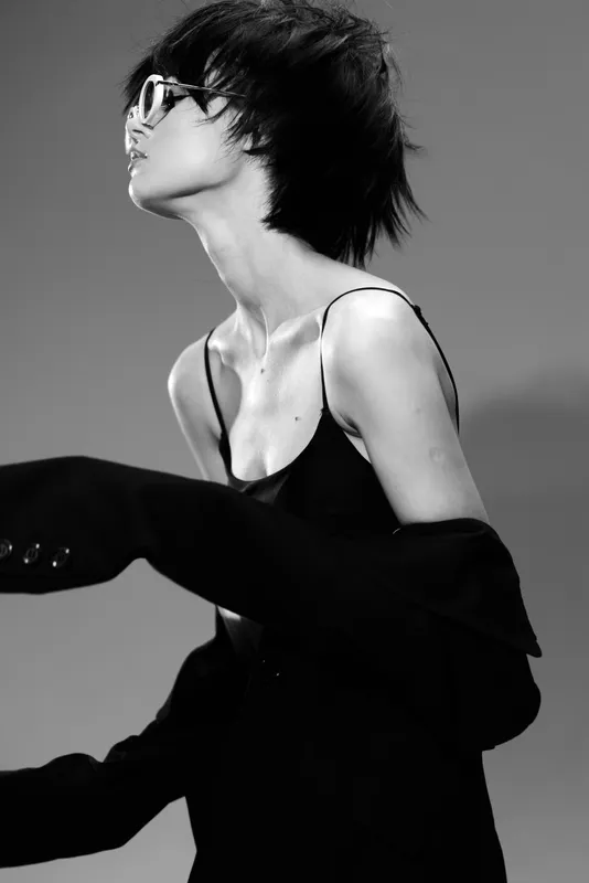 Stylish woman with short hair wearing sunglasses in black and white monochrome fashion pose.