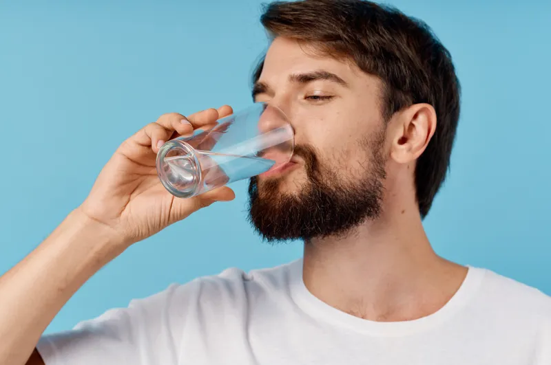 Крупный план красивого мужчины, пьющего воду из стакана на синем фоне