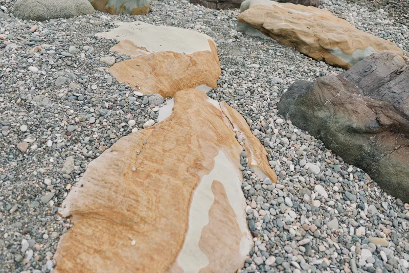 Close-up of large smooth beige rocks on a pebble beach. Natural textures and colors highlight the contrast between stone surfaces and small stones in a coastal environment.
