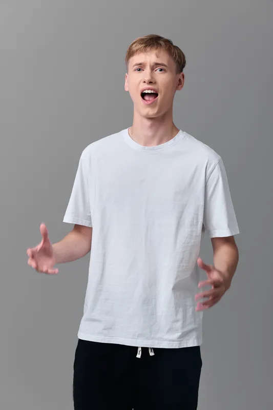 Yelling, surprised man with open mouth, dynamic gesture and white t shirt in a gray studio setting, conveying emotion, energy and attention for expressive reaction.