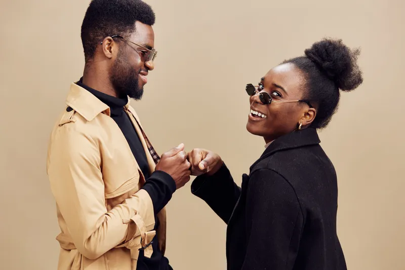 Happy couple having fun together, wearing stylish outfits and sunglasses, with a neutral background, capturing love and playfulness in a modern setting