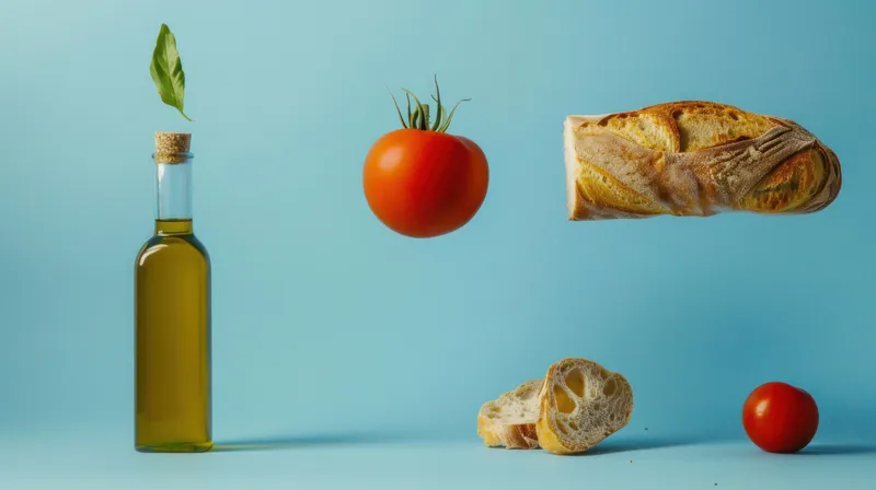 Стеклянная бутылка оливкового масла, целая и нарезанная буханка хлеба, а также красные помидоры на ярком голубом фоне