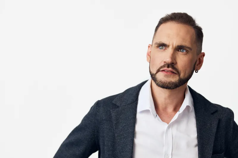A professional businessman stands against an isolated light background, projecting confidence and focus. He wears a blazer and white shirt, ready to discuss strategy and goals.