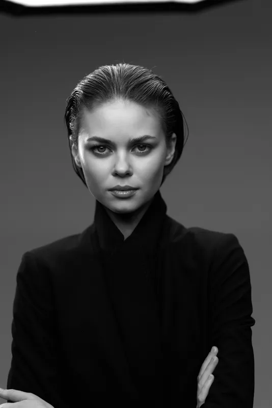 Black and white portrait of serious woman in dark clothing with intense gaze and minimalist background
