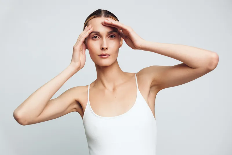 Woman portrait studio white tank hair hands beauty calm expression soft light on face clean background, natural confidence, grooming moment