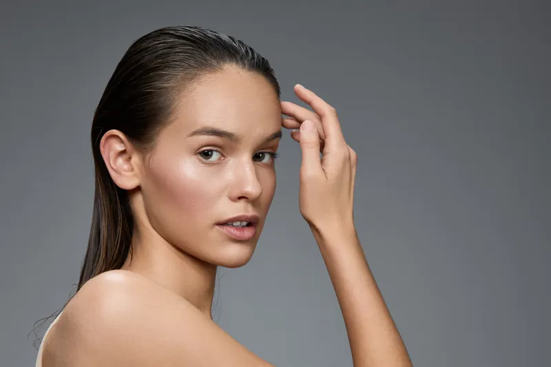 Young female model with long hair, minimal makeup, showcasing natural beauty and elegance against a neutral gray background, expressing confidence and serenity