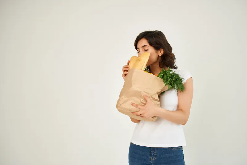 Женщина с пакетом продуктов делает покупки в супермаркете на светлом фоне