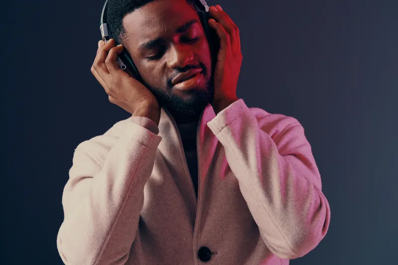 A young Black man enjoying music with headphones in a cozy sweater, displaying a relaxed emotion against a modern gradient background Perfect for music related themes