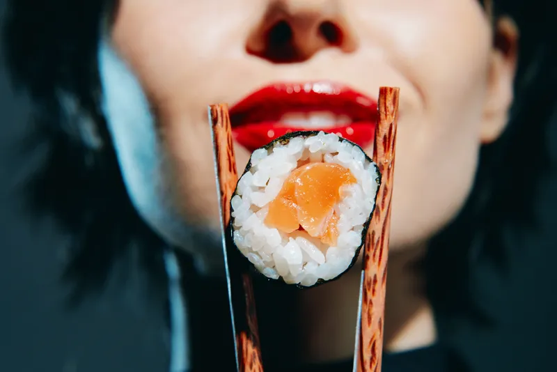 Стильная женщина держит суши палочками, демонстрируя чувство утончённости и наслаждения