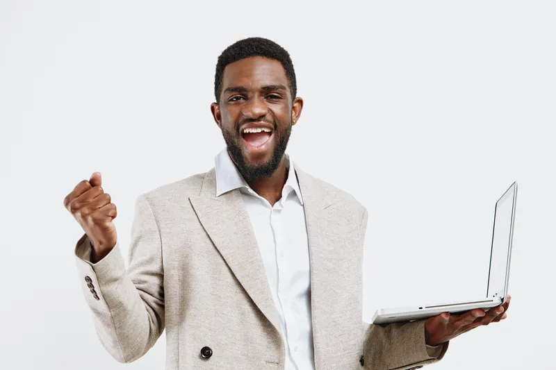 Smiling man with dark skin dressed in beige suit and white shirt holding laptop isolated on white background studio portrait. People lifestyle concept.