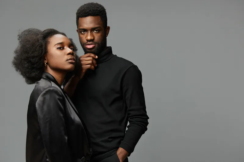Elegant African couple in stylish outfits, exuding confidence and charm against a neutral gray background, showcasing modern fashion