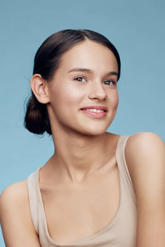 Young woman with natural makeup and a warm smile against a soft blue background, showcasing a fresh and healthy look, ideal for beauty and wellness concepts