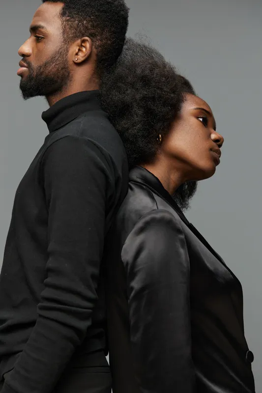 Stylish couple in modern attire showcasing emotion and connection, featuring dark clothing against a muted background, embodying elegance and sophistication