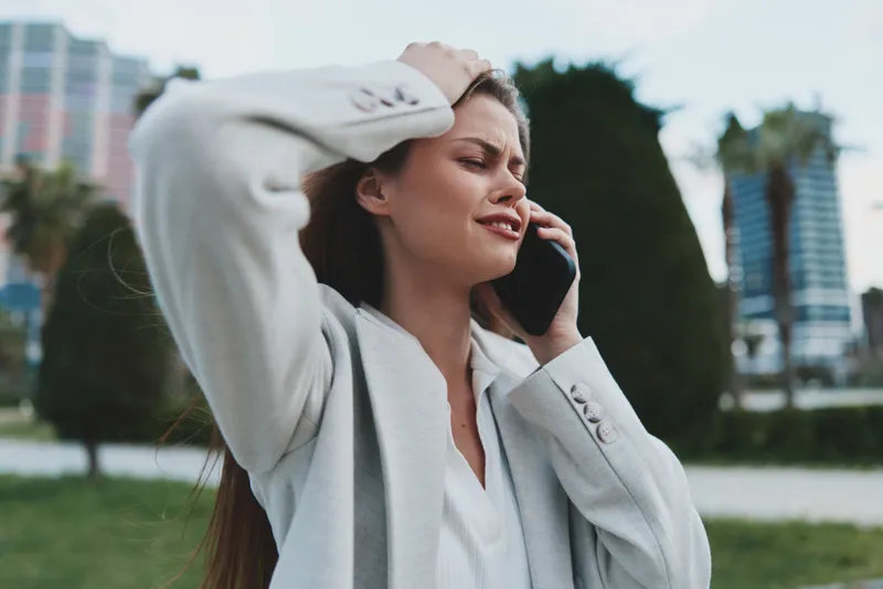 Woman stressed on phone call with urban background expressing financial crisis and anxiety in business casual outfit NAME: Woman stressed on phone call with urban background expressing financial crisi