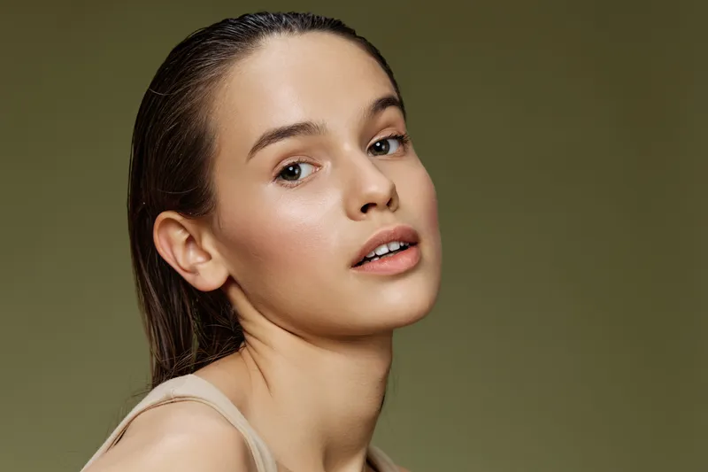 Natural beauty portrait of a young woman with fair skin and wet hair, emphasizing a fresh and radiant look against a soft green background