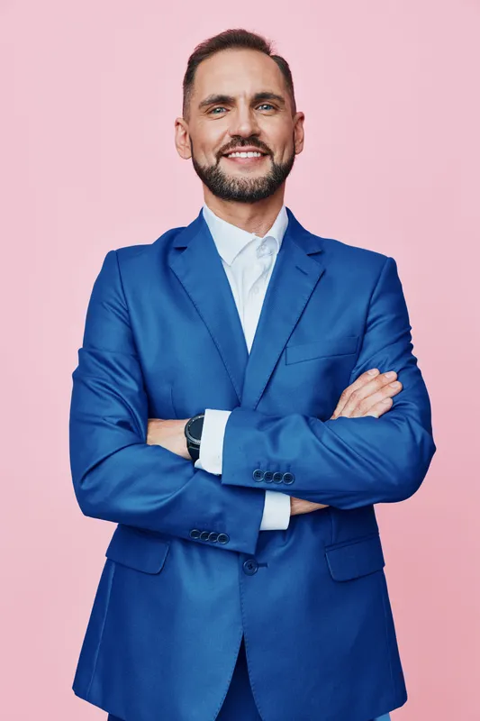 A professional businessman stands against a solid pink background, projecting confidence with a calm smile and poised posture, ready for leadership, collaboration, and effective communication in any