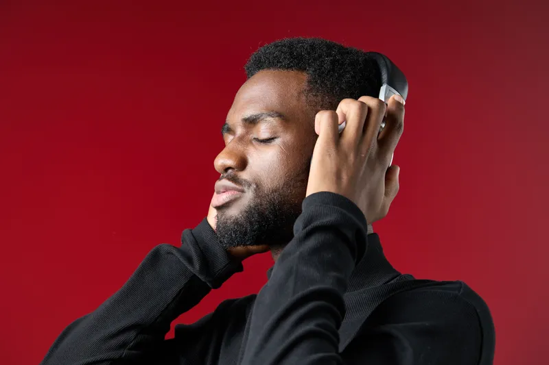 Young Black man enjoying music with headphones against a vibrant red background, expressing joy and relaxation through music