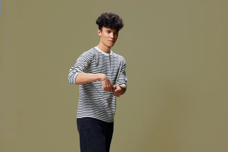 young man in striped shirt posing confidently against plain olive background, casual style and relaxed mood with modern hairstyle
