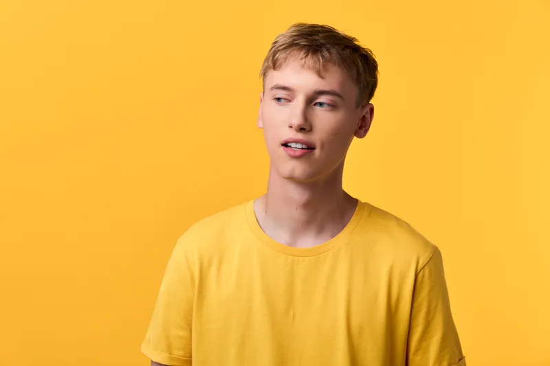 Young man wearing a yellow shirt against a bright yellow background, casual style and relaxed expression, simple fashion mood, studio look without branding